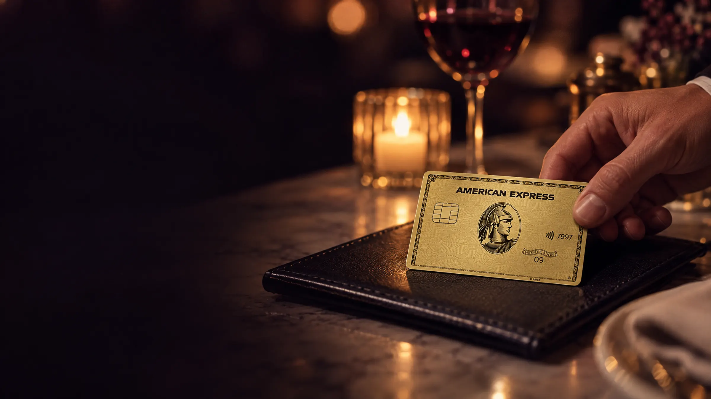 A hand laying an American Express Gold Card on a restaurant check