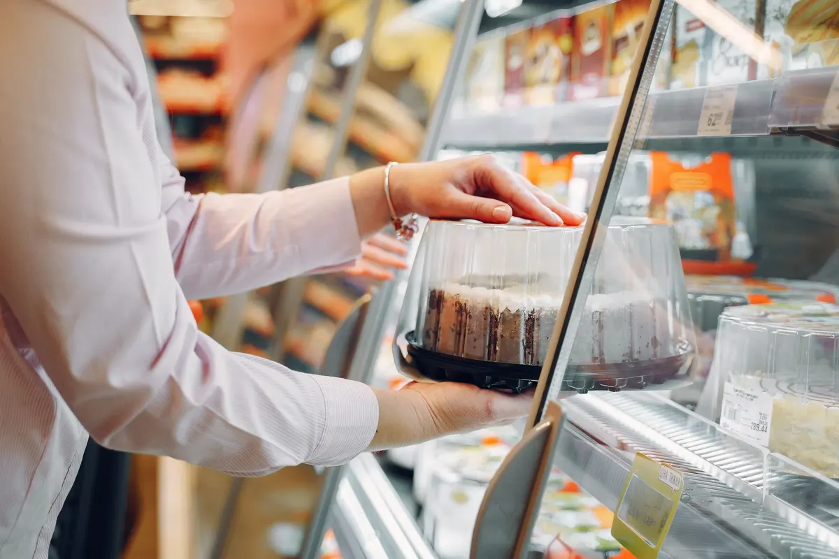 A shopper lifting a cake from a supermarket chiller