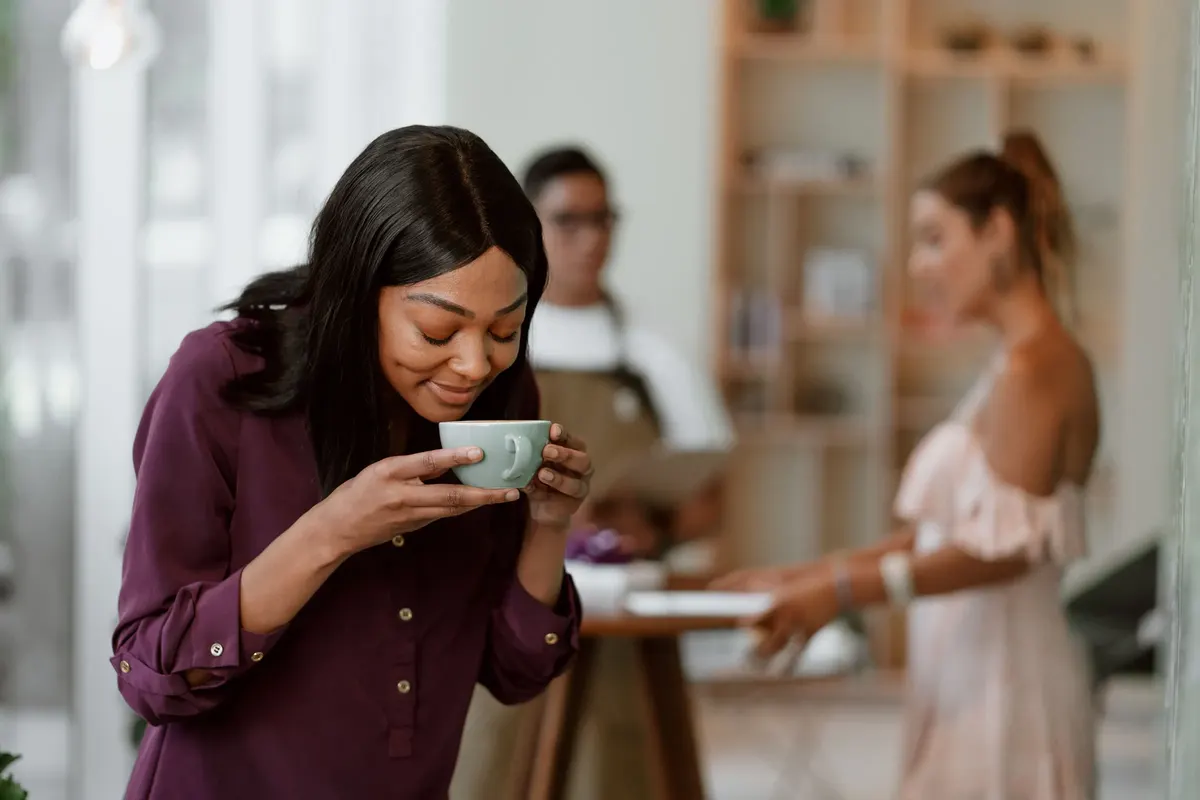 A woman with her eyes closed, smelling a cup of coffee
