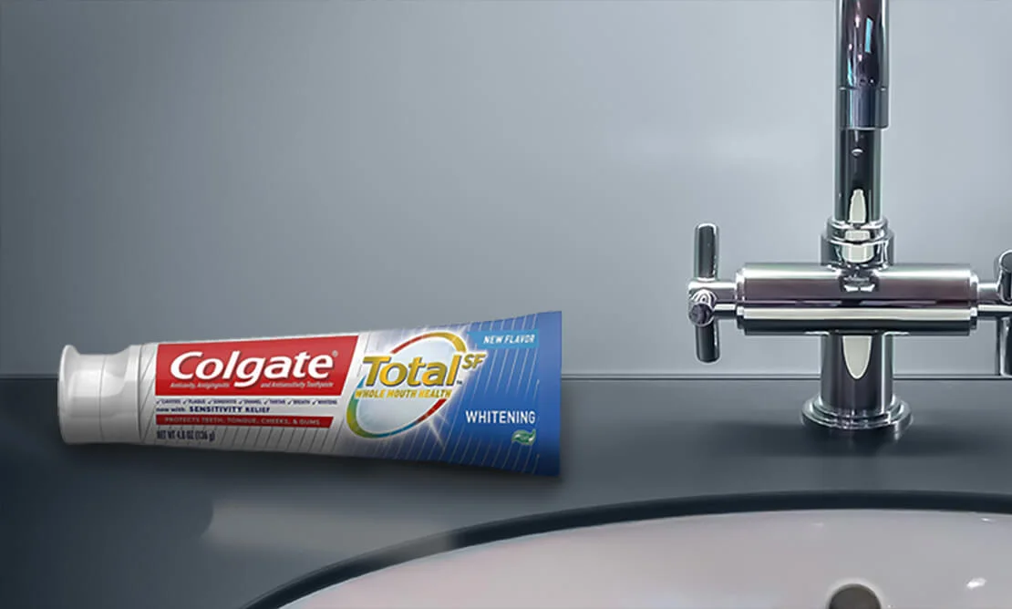 A tube of Colgate Total beside a bathroom faucet