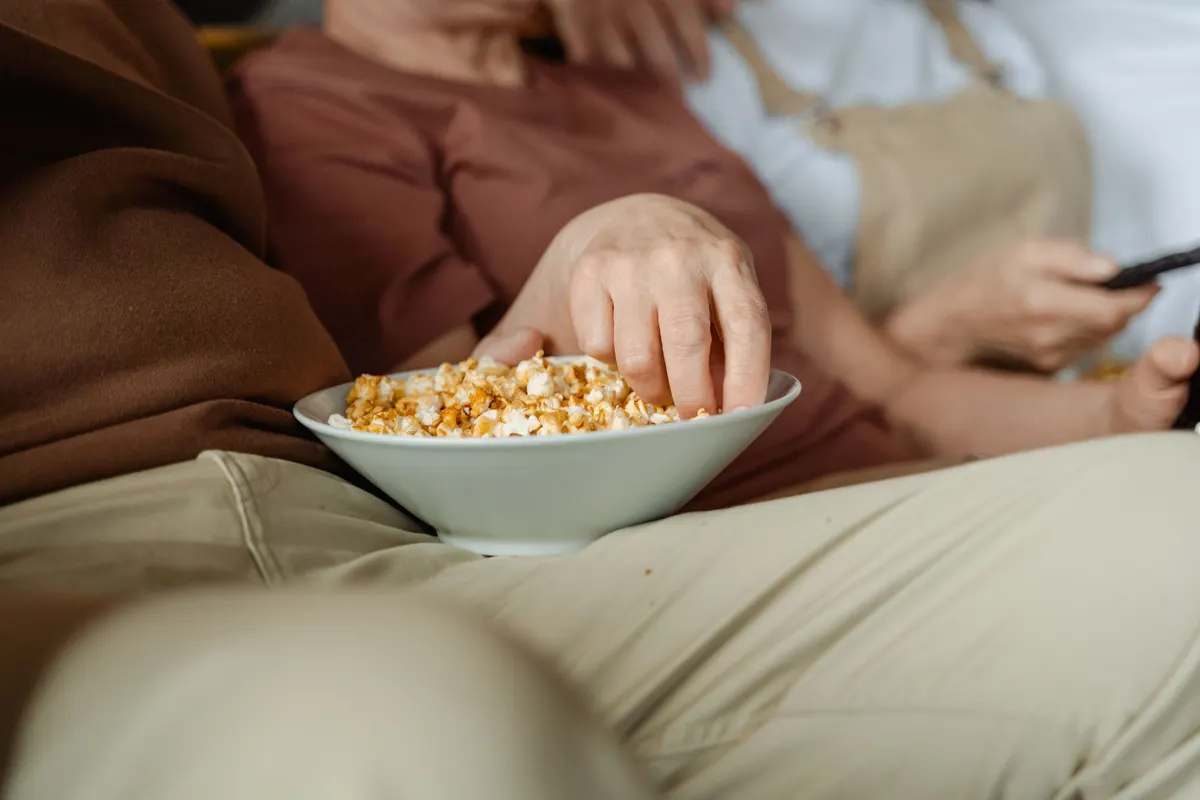 A hand reaching into a bowl of popcorn on a sofa