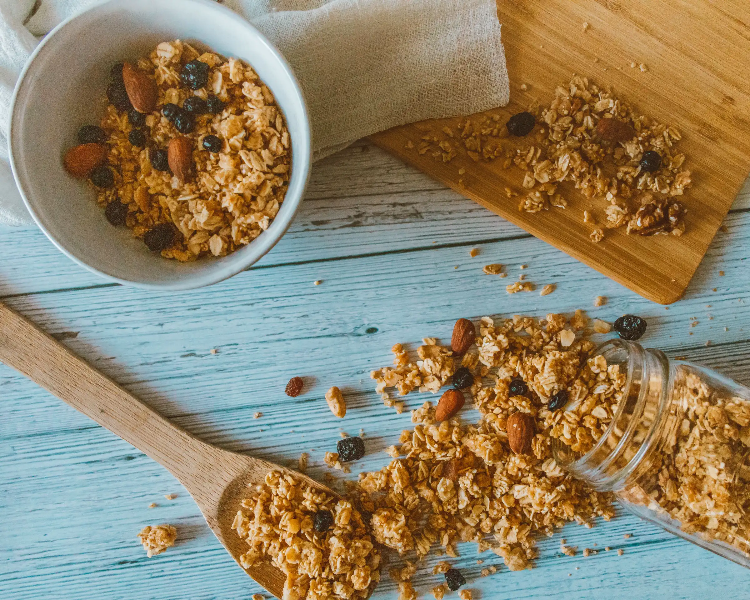Granola with almonds and raisins, spilled from a jar onto a wooden table