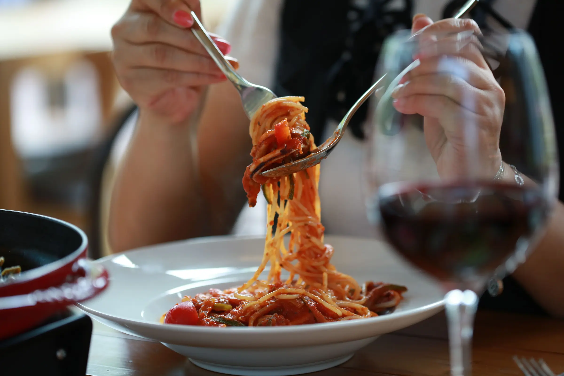 A forkful of spaghetti in tomato sauce, with a glass of red wine