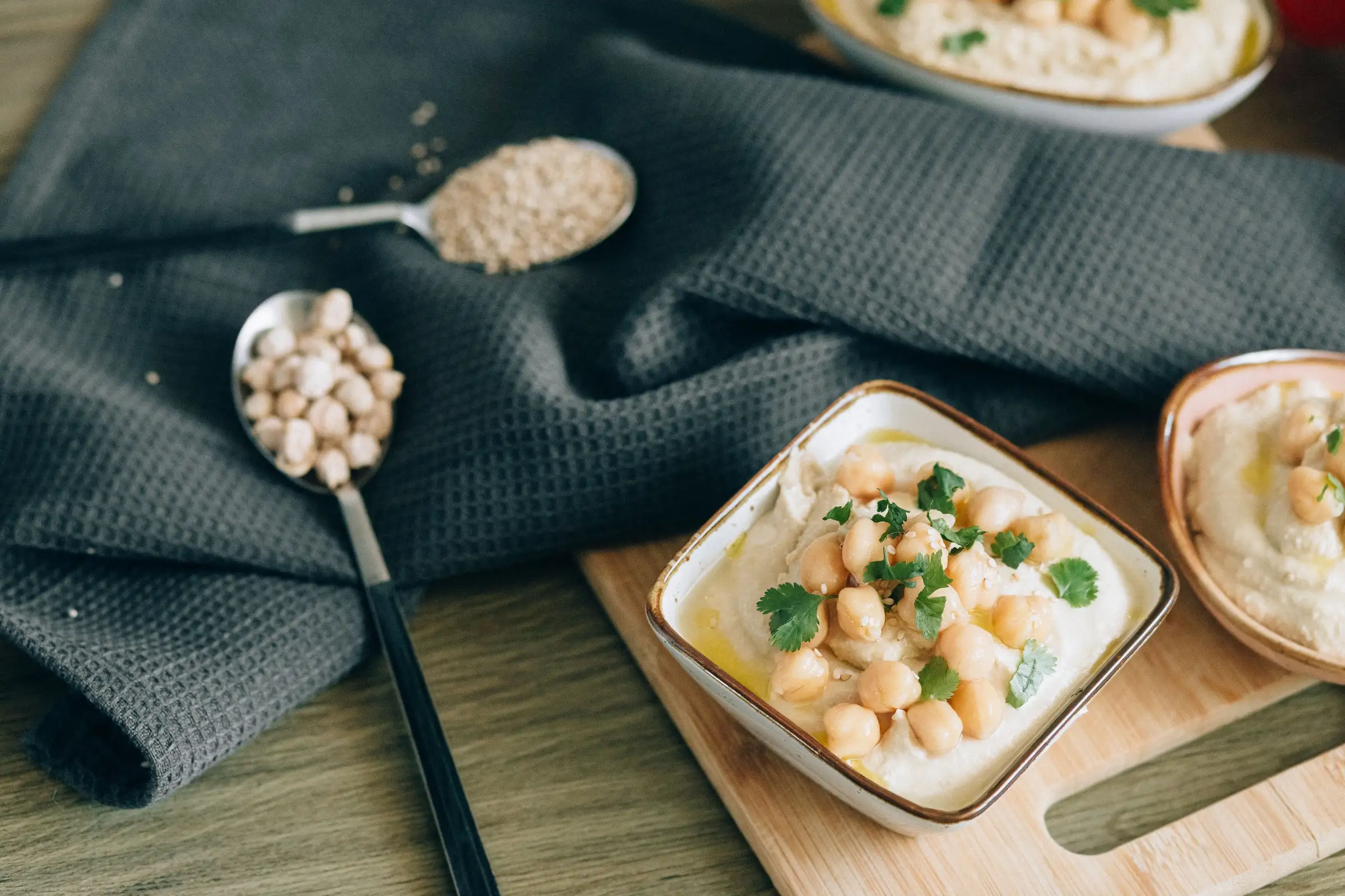 Hummus topped with chickpeas and parsley, on a wooden board