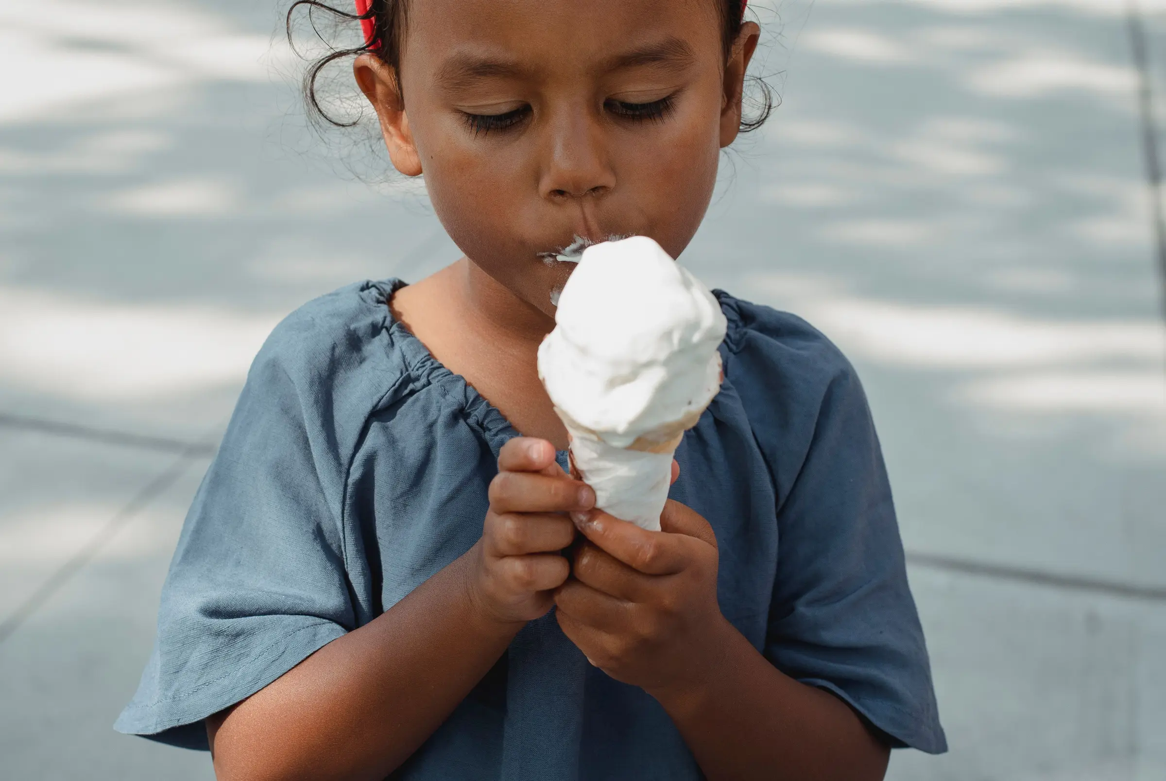 A girl with her eyes closed, eating an ice cream cone